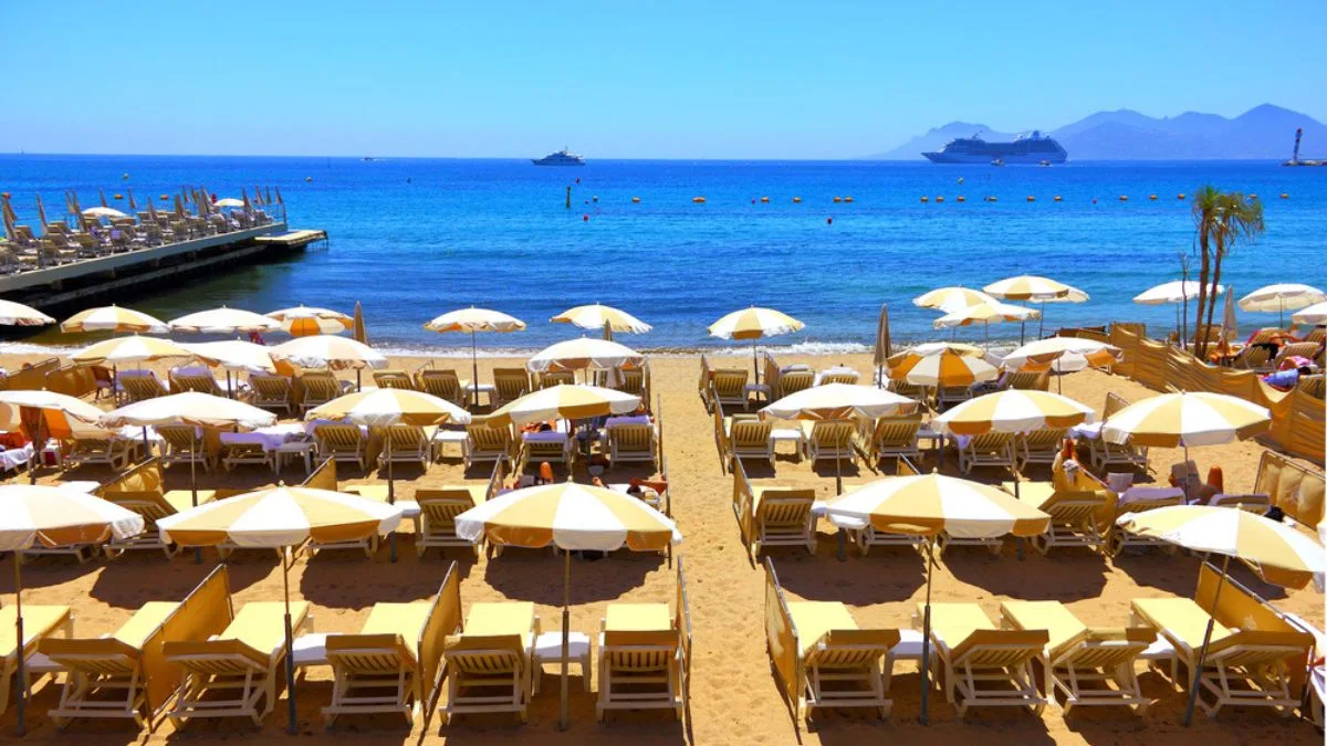 view over Cannes beach bar with sunloungers and sea and cruise ship in the distance